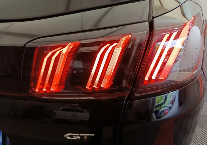 Gros plan sur les feux arrière rouges du côté gauche d’un Peugeot 3008 noir version GT.