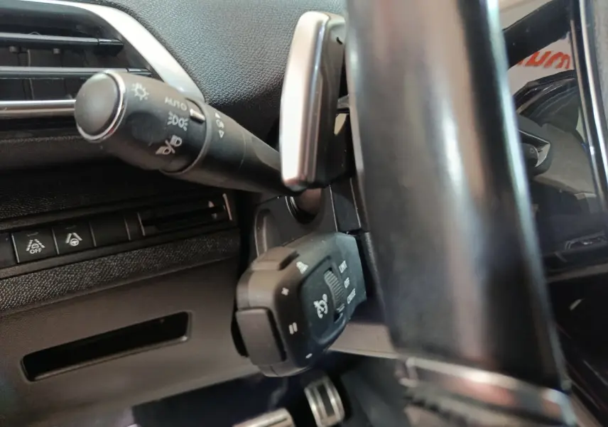 Gros plan sur la colonne de direction et commandes au volant du Peugeot 3008 noir, intérieur avec volant cuir.