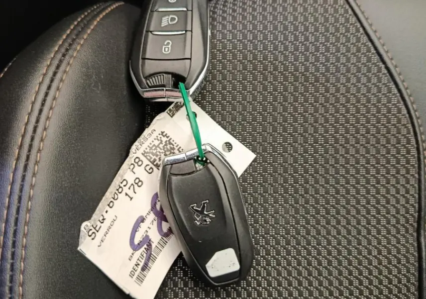 Gros plan sur les clés noires de Peugeot 3008 PureTech posées sur un siège tissu noir avec surpiqûres marron.