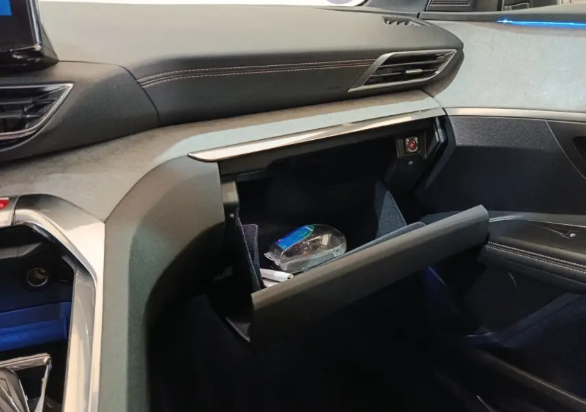 Intérieur côté passager du Peugeot 3008 GT 2022 noir, boîte à gants ouverte avec objets visibles et éclairage d'ambiance bleu.