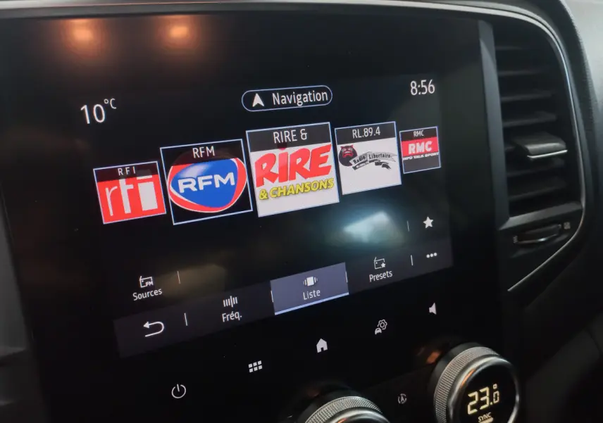 Écran tactile central de la Renault Mégane Business blanc, affichant les stations radio avec commandes climatisation en dessous.