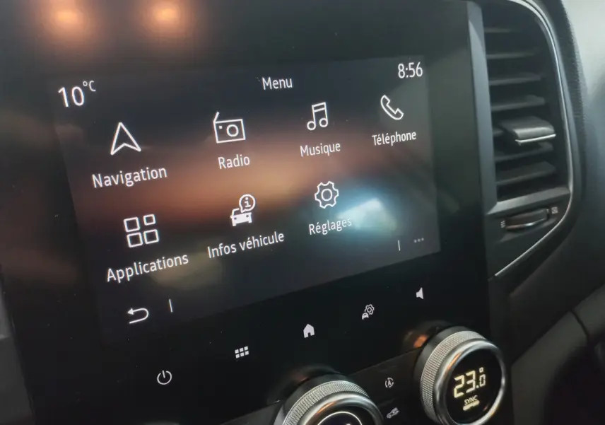 Écran tactile central affichant menu multimédia et climatisation digitale dans Renault Mégane Business blanc, vue de face rapprochée.