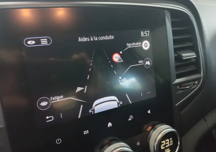 Écran tactile central de la Renault Mégane Business blanc, affichant les aides à la conduite et la climatisation à 23°C.