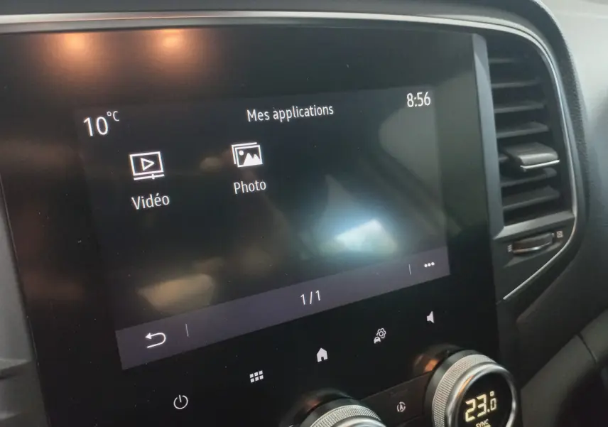 Écran tactile central affichant les applications vidéo et photo, avec commandes de climatisation digitale sur Renault Mégane blanche.
