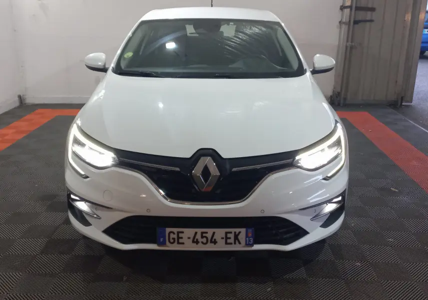 Vue frontale d'une Renault Mégane blanche 2022 avec phares LED allumés dans un garage.