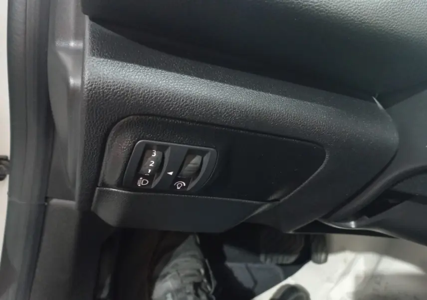 Gros plan sur les commandes de réglage des phares et du tableau de bord dans une Renault Mégane Business blanche, côté conducteur.