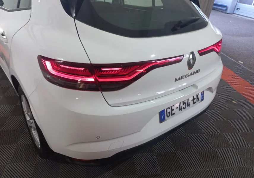 Vue 3/4 arrière droite d'une Renault Mégane blanche 2022 avec feux arrière LED allumés et plaque française visible