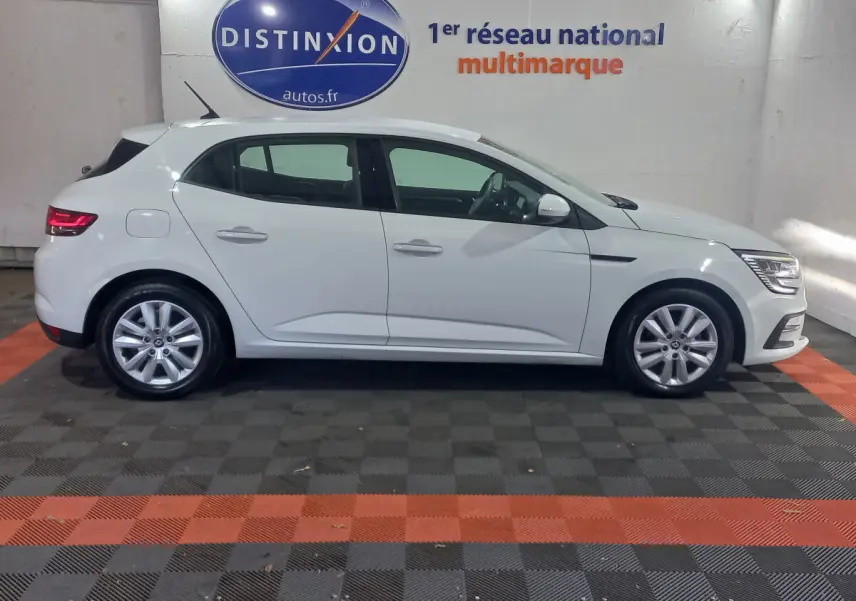 Profil droit d'une Renault Mégane Business Blue dCi 115 EDC blanche, stationnée en intérieur sur sol damier noir et orange.