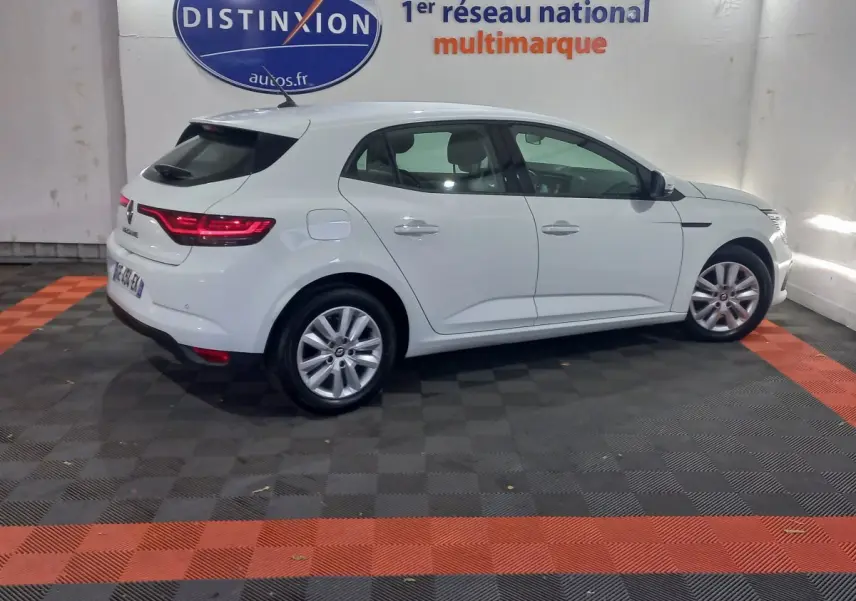 Vue latérale droite d'une Renault Mégane Business Blue dCi 115 blanche, avec feux arrière LED allumés, en intérieur showroom.