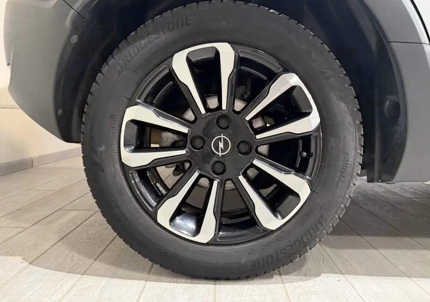 Gros plan sur la roue avant droite d’un Opel Crossland gris, jante alliage noire et argent avec logo Opel central.