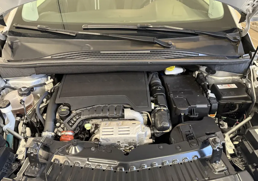 Vue rapprochée du moteur essence gris de l'Opel Crossland 1.2 Turbo 110 ch avec capot ouvert, montrant les composants mécaniques.