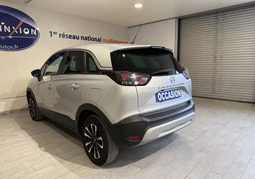 Vue 3/4 arrière droite d'un Opel Crossland gris 2023 avec toit noir et feux arrière fumés en intérieur showroom.