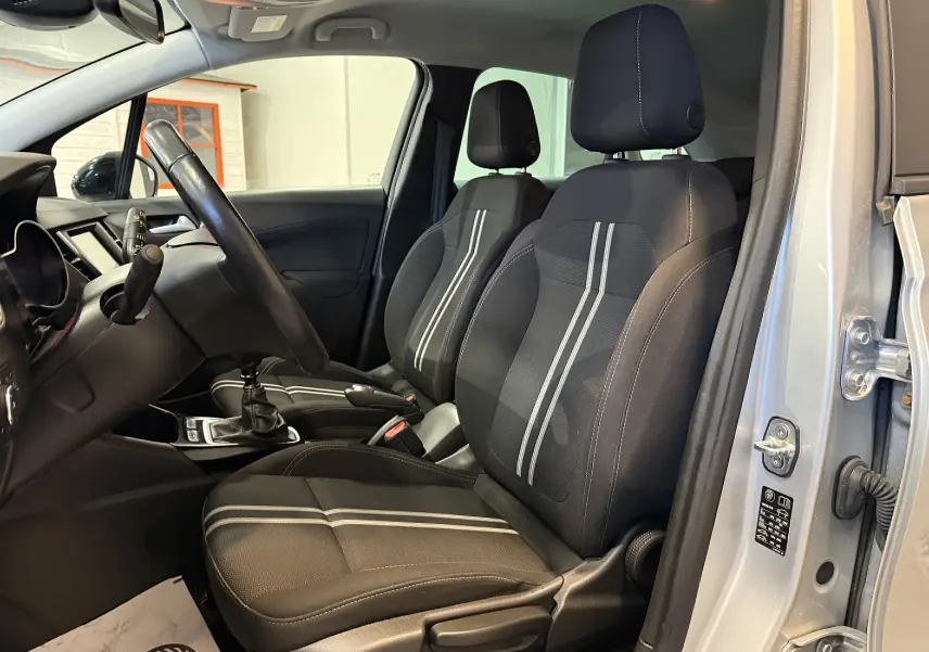Vue intérieure côté conducteur de l’Opel Crossland gris 2023, montrant les sièges noirs avec bandes grises et la boîte manuelle.