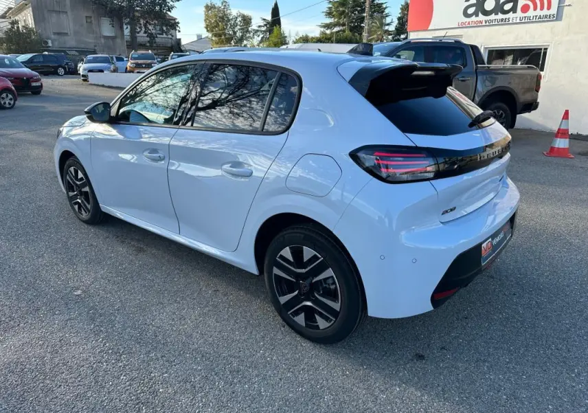 Peugeot 208 Hybrid blanc vue 3/4 arrière droit, jantes alliage noires, feux arrière LED et antenne requin visible.