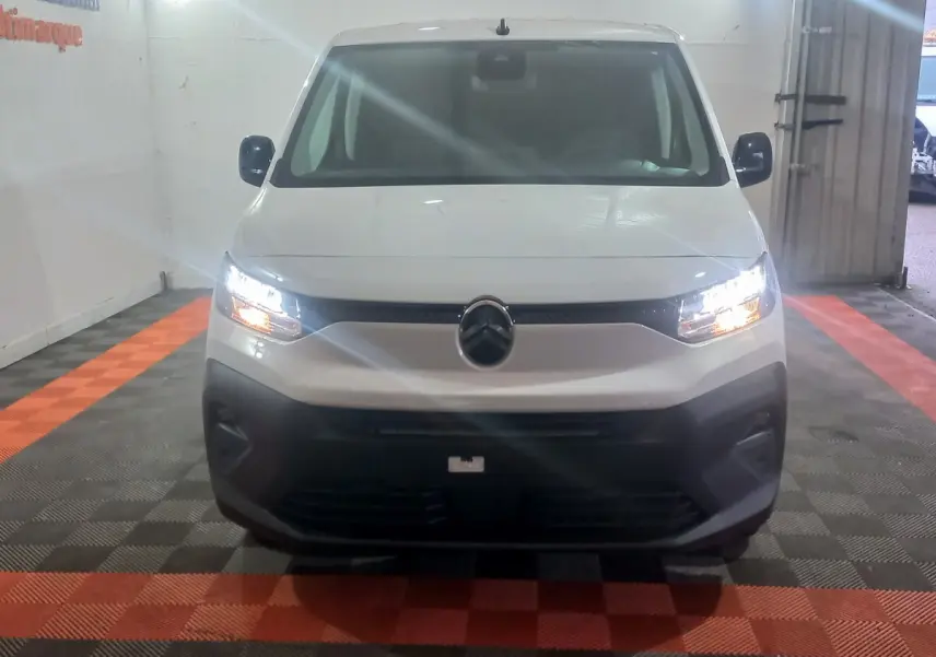 Vue frontale d’un Citroën Berlingo XL blanc 2025 avec phares allumés et bouclier noir dans un garage.
