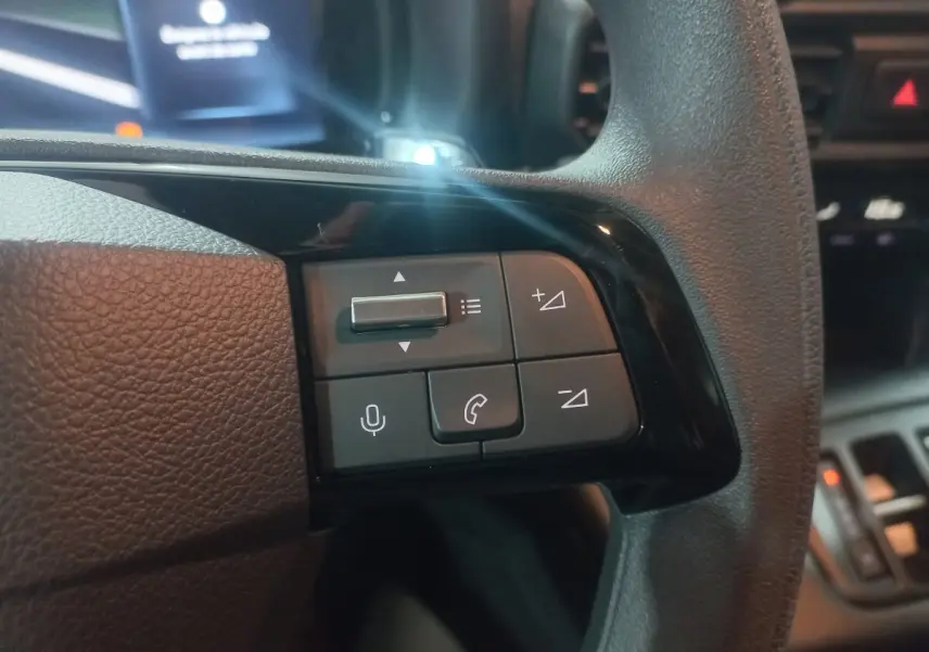 Gros plan sur les commandes multifonctions noires du volant côté gauche du Citroën Berlingo XL 2025, intérieur sombre.