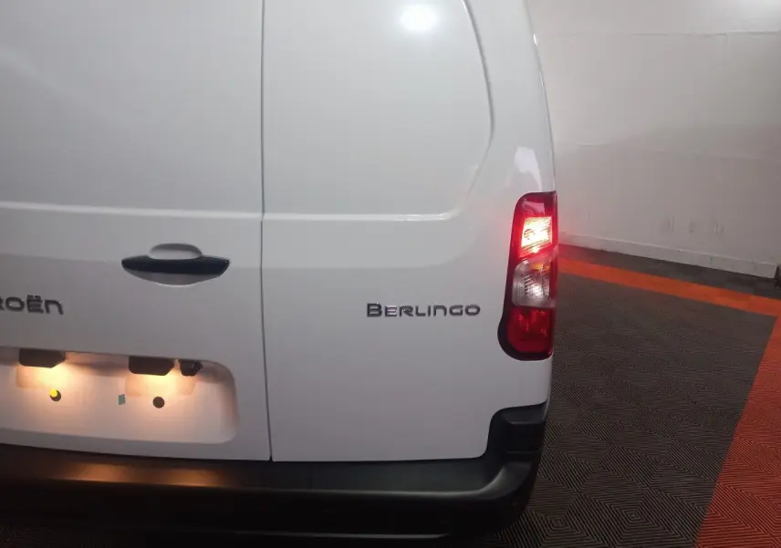Vue arrière droite du Citroën Berlingo blanc avec feu arrière allumé dans un garage au sol noir et orange.