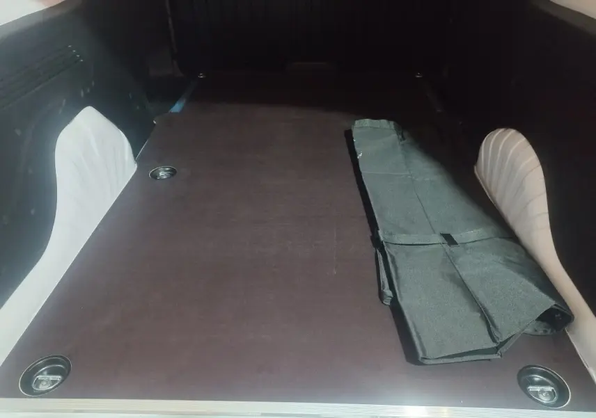 Vue intérieure du coffre du Citroën Berlingo XL blanc 2025, montrant l'espace de chargement plat avec un tapis noir plié.