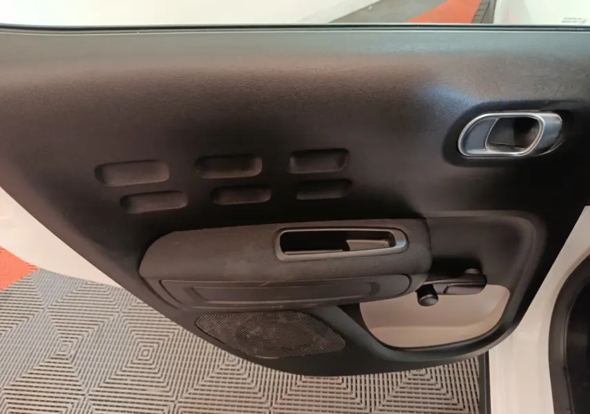 Vue rapprochée de la porte avant gauche noire et blanche de la Citroën C3 avec poignée et commande de vitre manuelle.