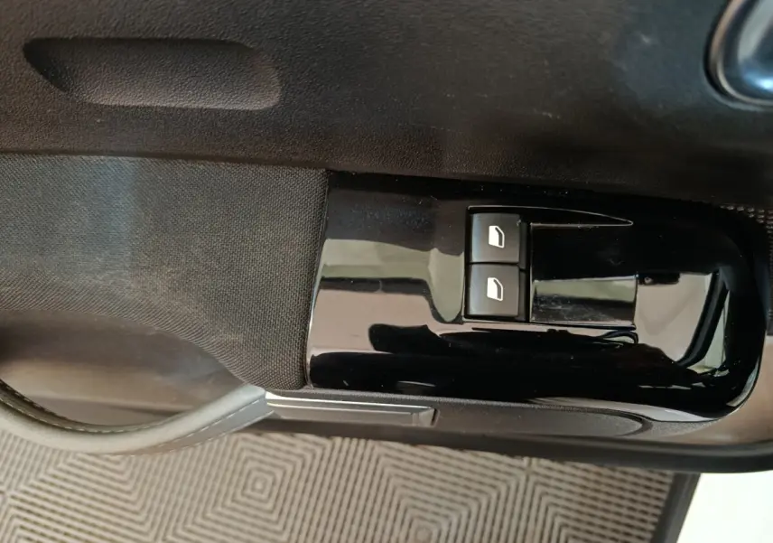 Gros plan sur les commandes de lève-vitres avant gauche en plastique noir brillant dans une Citroën C3 blanche de 2021.