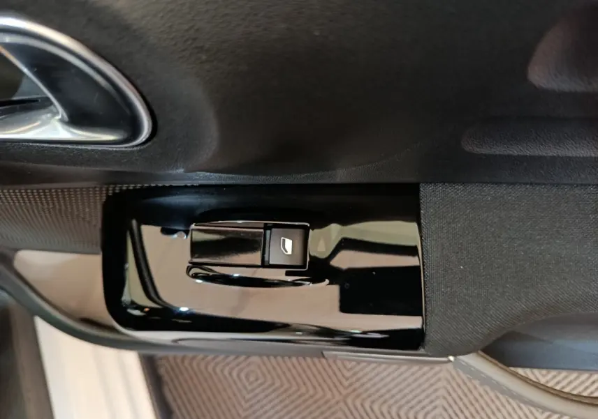 Gros plan sur le bouton de commande de la vitre électrique côté conducteur d'une Citroën C3 blanche.