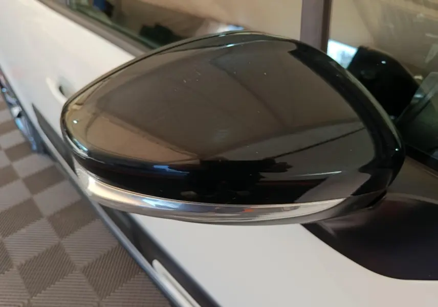 Gros plan sur le rétroviseur noir côté gauche d'une Citroën C3 blanche vue de profil, avec clignotant intégré.