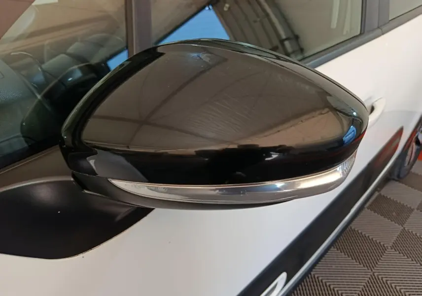 Gros plan sur le rétroviseur noir côté gauche d'une Citroën C3 blanche, avec clignotant intégré.