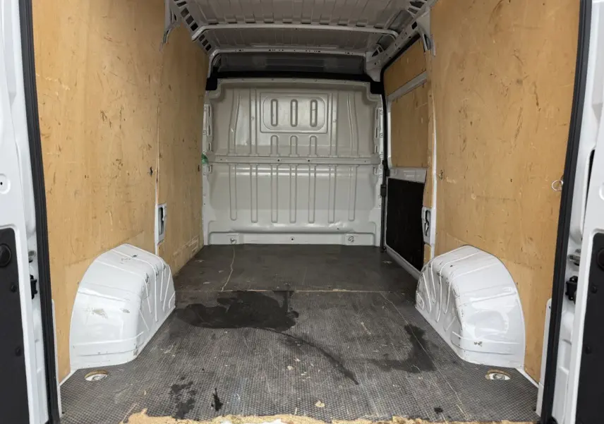 Vue intérieure arrière du fourgon blanc Peugeot Boxer 2.2 140 CH avec parois en bois et sol noir usé.