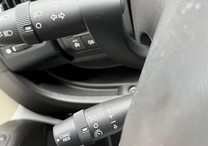 Gros plan sur les commandes de volant multifonctions noir du Peugeot Boxer Fourgon blanc, côté gauche du poste de conduite.