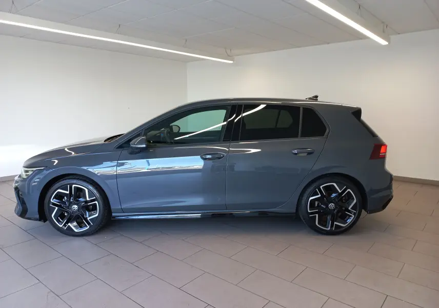 Profil gauche d'une Volkswagen Golf 1.5 eTSI 150 DSG7 R-Line Edition gris dauphin avec jantes noires et détails sportifs.