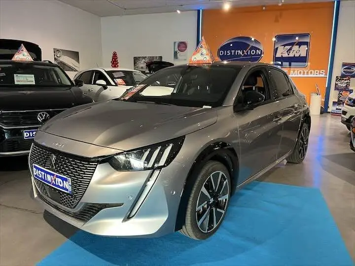 Peugeot e-208 GT gris Artense vue 3/4 avant droit en showroom avec jantes alliage et calandre distinctive.