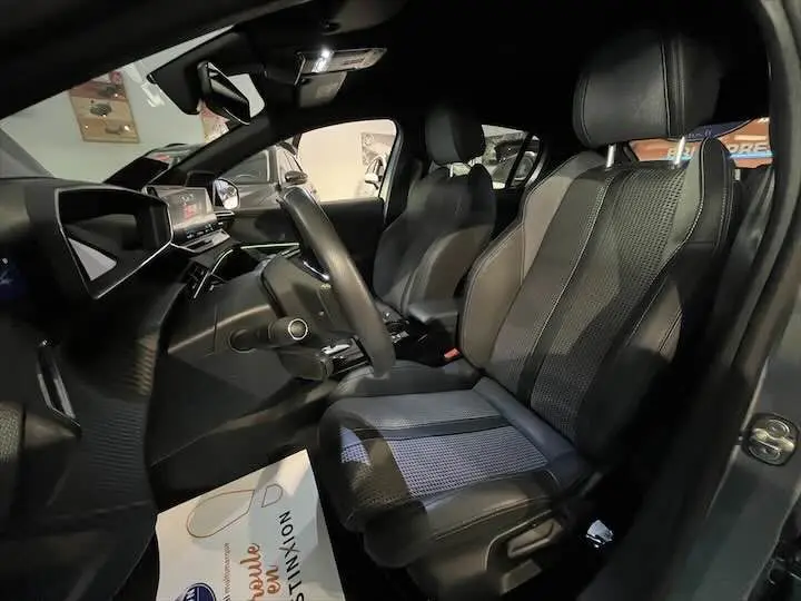Intérieur de la Peugeot e-208 GT 2022, vue côté conducteur, sièges en cuir noir avec inserts tissu gris et tableau de bord moderne.