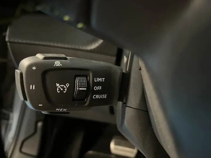 Gros plan sur la commande de régulateur de vitesse de la Peugeot e-208 GT 2022, intérieur noir.