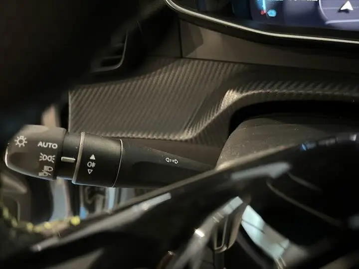 Gros plan sur la commande des feux et clignotants dans l'habitacle sombre d'une Peugeot 208 électrique gris Artense.