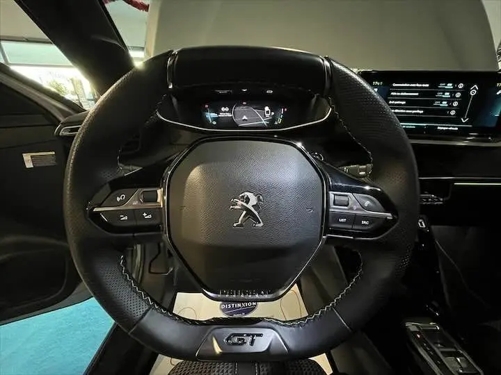 Gros plan sur le volant cuir noir de la Peugeot e-208 GT 2022 avec logo lion et tableau de bord numérique visible.