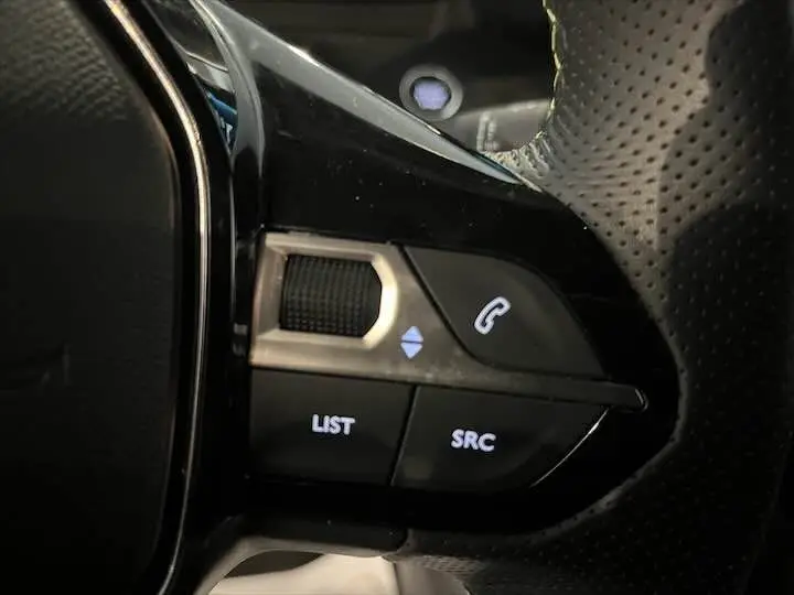 Gros plan sur les commandes noires du volant perforé de la Peugeot 208 E-208 GT gris Artense.