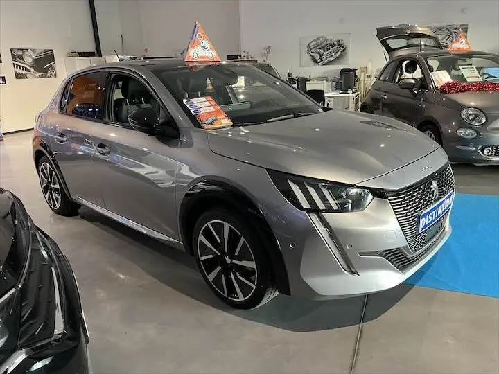 Peugeot 208 électrique gris Artense vue 3/4 avant droit en showroom avec jantes noires et grises.