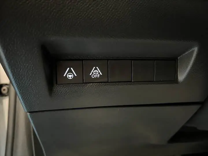 Boutons de contrôle d'aide à la conduite avec symboles blancs sur fond noir dans l'habitacle d'une Peugeot e-208 gris Artense.
