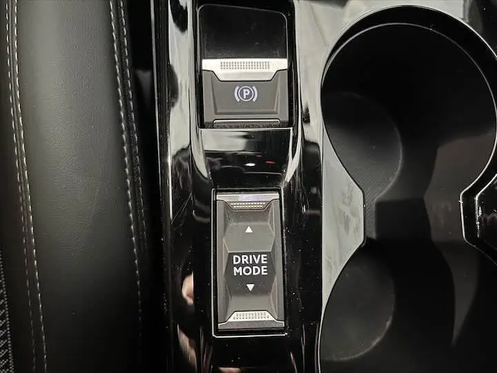 Gros plan sur la console centrale noire de la Peugeot e-208 GT avec bouton Drive Mode et frein à main électrique.