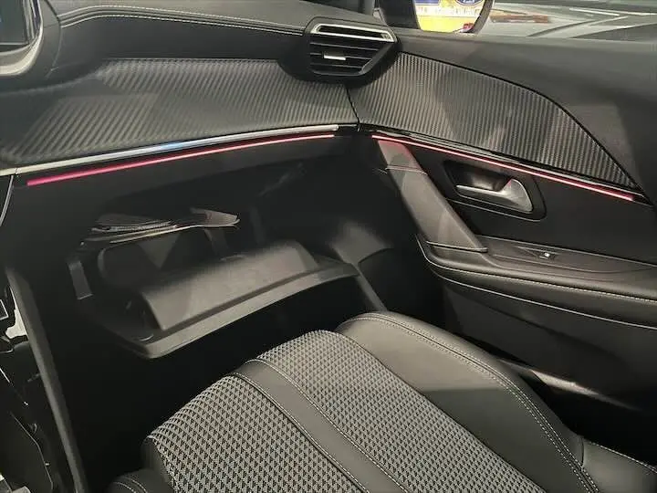 Intérieur côté passager de la Peugeot e-208 GT 2022, montrant la boîte à gants ouverte et la finition cuir noir avec éclairage d'ambiance rose.