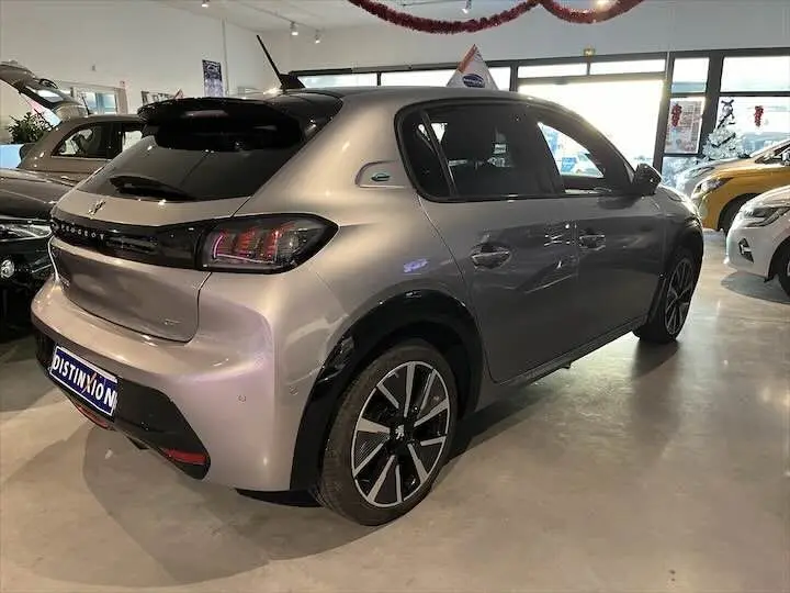 Vue 3/4 arrière droite d'une Peugeot e-208 GT électrique gris Artense en showroom avec jantes noires et détails noirs brillants.