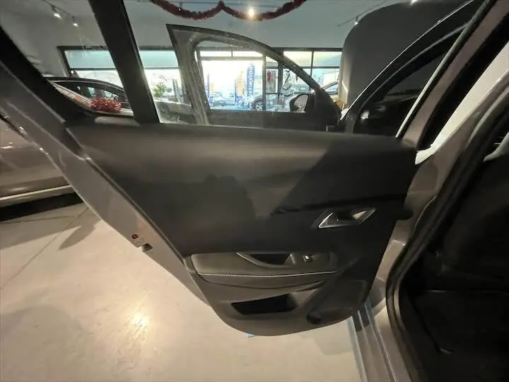 Porte arrière gauche ouverte de la Peugeot 208 E-208 GT gris Artense, montrant l'habillage intérieur noir avec commandes de vitre.