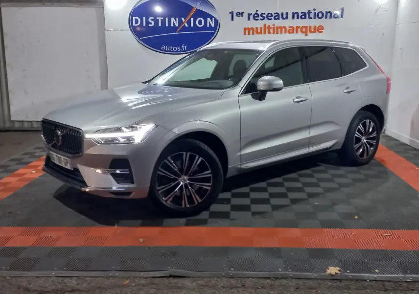 Volvo XC60 B4 gris clair vu de 3/4 avant droit, avec jantes alliage et phares LED allumés en intérieur showroom.