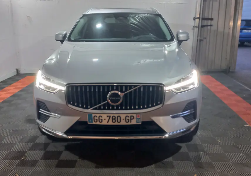 Vue frontale d'un Volvo XC60 gris clair 2022 avec phares LED allumés dans un garage fermé.