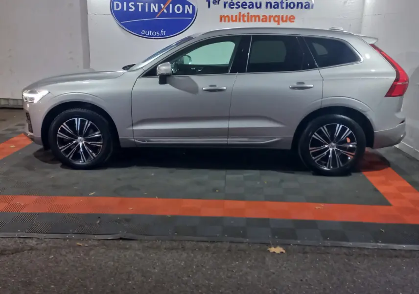 Profil côté gauche d'un Volvo XC60 gris clair 2022 garé en intérieur avec jantes noires et chromées visibles.