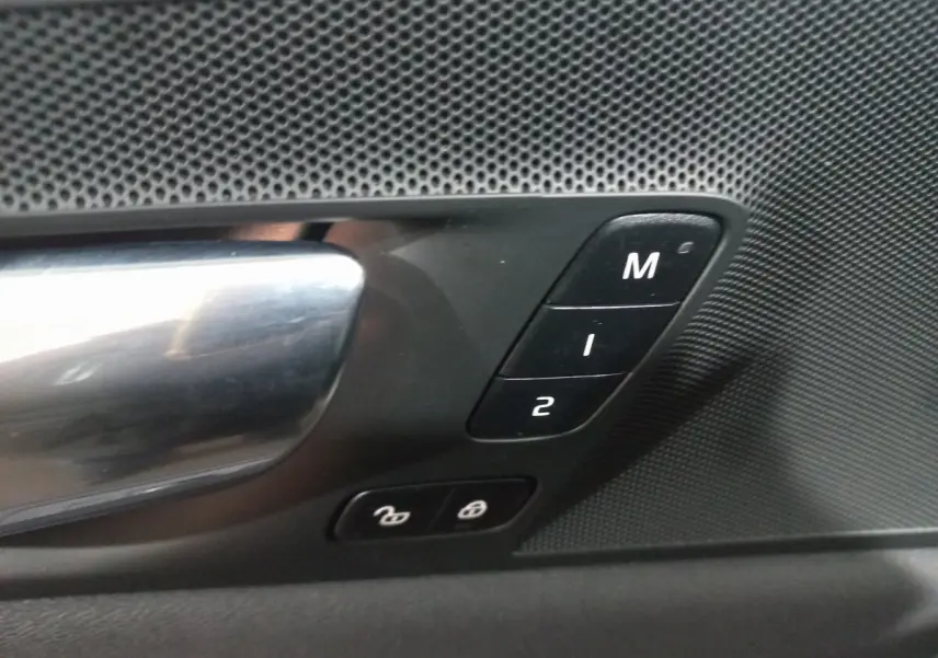 Gros plan sur la poignée intérieure côté gauche du Volvo XC60 gris clair avec boutons mémoire et verrouillage des portes.