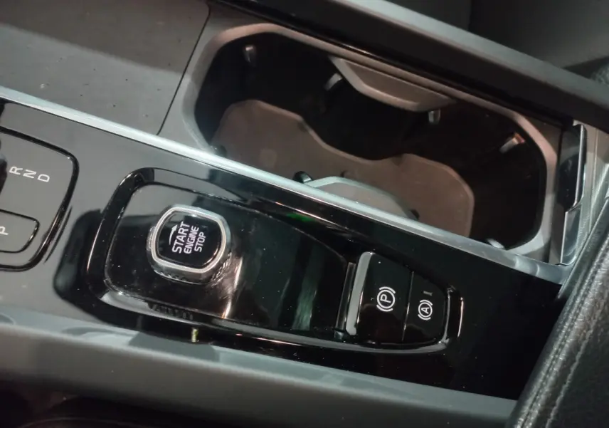 Gros plan sur la console centrale noire brillante du Volvo XC60 B4 197 Geartronic, avec bouton start/stop et commandes parking.