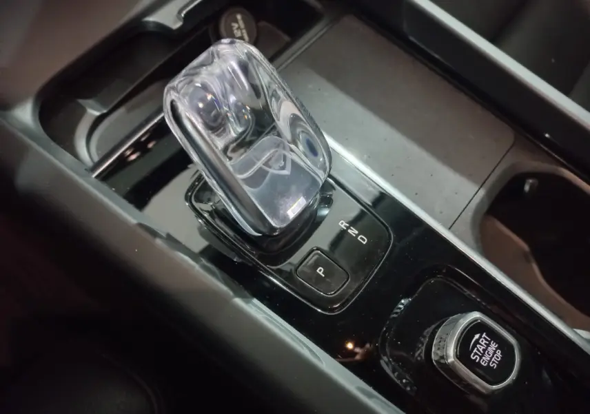 Le levier de vitesses transparent et le bouton start/stop du Volvo XC60 B4 gris clair vus en gros plan sur la console centrale.