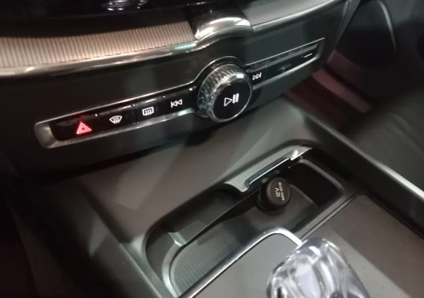Gros plan sur la console centrale noire du Volvo XC60 B4 2022, avec bouton d'alerte rouge et prise 12V visible.