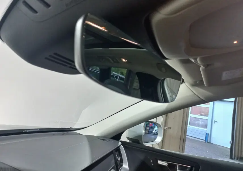 Vue intérieure du rétroviseur central et du tableau de bord noir du Volvo XC60 gris clair, côté droit visible par la fenêtre ouverte.